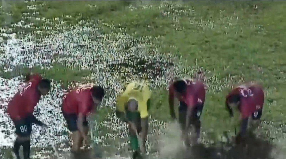 Com rodos, jogadores tentam tirar água de campo de futebol no ES — Foto: Reprodução